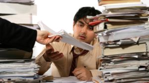 Frustrated office worker starting at piles of unorganized paper documents on a desk