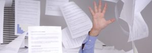 A hand emerging from a massive pile of printed documents