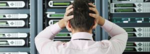 An IT professional staring at a row of network servers with his hands on his head in frustration