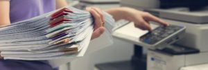 A woman holding a stack of documents at a copy machine