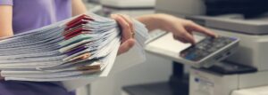 Woman at a scanner holding a stack of papers