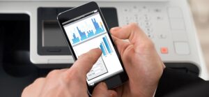 man at printer looking at document on smartphone