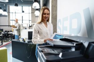 Woman stands over an office copier holding an output that was just printed