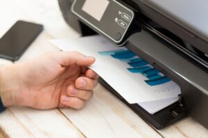 close up of a man's hand getting colorful chart print-outs from a business printer
