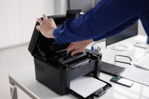 A technician performing copier maintenance by opening the lid of a copier machine to inspect its components. This image highlights the importance of regular copier maintenance to ensure optimal performance and longevity of office equipment.