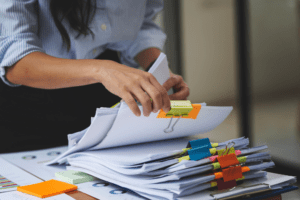 Close-up of a professional organizing a stack of documents using colorful binder clips and sticky notes, symbolizing efficient and structured processes for Document Management in an office setting.