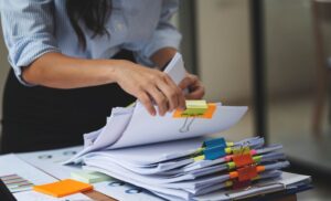 A professional woman organizing paperwork with colorful binder clips and sticky notes on a desk, representing efficient document management in an office setting.v