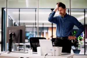 Frustrated employee in an office stetting standing above a printer signifying the need for printer maintenance.