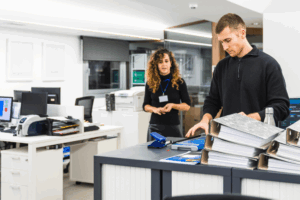 Two employees in an office copier room addressing papers to symbolize the importance of MPS.
