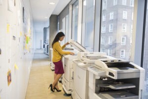 Full length of businesswoman using photocopier copier and printer leases near me