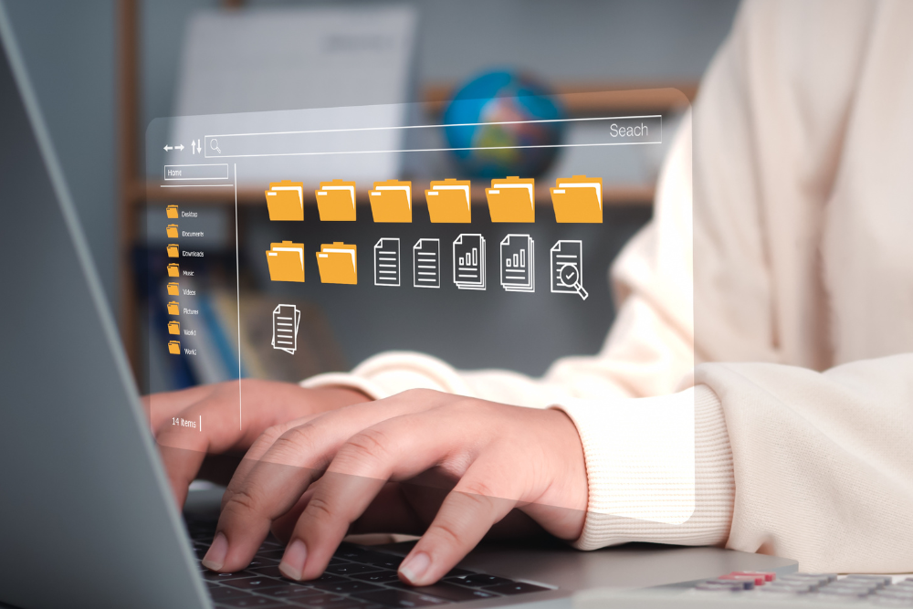 Close up of hands typing on a laptop in the foreground and a globe on a shelf in the background. Above the hands are icons within the file search feature, with folders and document icons on the screen, as a conceptual representation of digital records management.